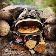 a pizza sitting on top of a metal grill next to rocks and logs in the woods