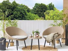 two wicker chairs sitting next to each other on a wooden floor in front of a white fence