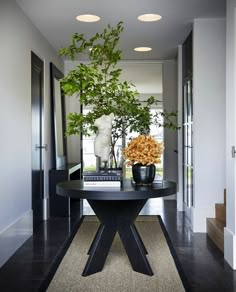 a black table topped with a vase filled with flowers next to a plant on top of a hard wood floor