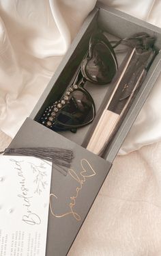 a pair of sunglasses in a gift box on a white bed with a note and pen