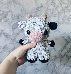 a hand holding a small crocheted cow on top of a marble countertop