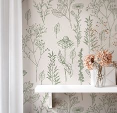 a vase with flowers on a shelf in front of a wallpapered wall and white curtains