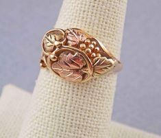 "Size 6-1/2 solid gold ring in a timeless openwork leaves & vines pattern, from Black Hills Gold manufacturer Landstrom's. This is a pre-owned ring; it has few very light scratches consistent with normal use, no bends or damage. Weighing just under 4 grams pure 10K band and 12K leaves, ring has a pleasing feel.  Gently domed face displays a blend of varying size rose & green gold leaves with a cluster of yellow gold grapes to one side, all surrounded by openwork twining vines with see-through ar Personalized Jewelry For Mom Bracelet Black Hills Gold, Black Hills Gold Heart Necklace, Black Hills Gold Rings Vintage, Collectible Art Nouveau Yellow Gold Ring, Black Hills Gold Rings, Black Hills Gold Jewelry, Black Hills Gold, Gold Alloys, Green Rose