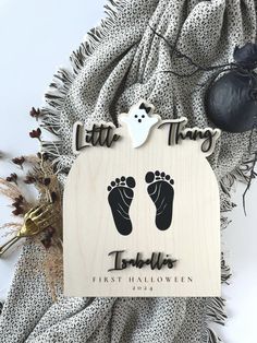 a wooden ornament with two baby feet and a ghost on it, sitting next to a blanket