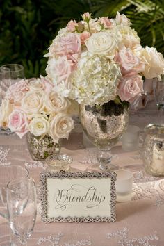 a table topped with lots of white and pink flowers on top of a lace covered table cloth