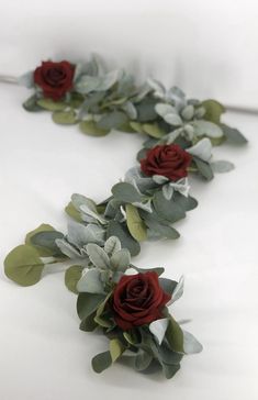 red roses and greenery are arranged on a white surface