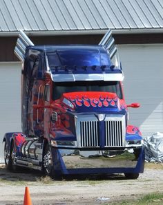 a red and blue semi truck parked in front of a building with an orange cone next to it