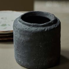 a black vase sitting on top of a table next to a plate