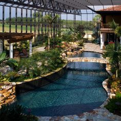 an outdoor swimming pool surrounded by greenery and rocks with a pergolated roof