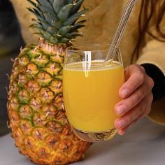 a person holding up a glass of juice next to a pineapple