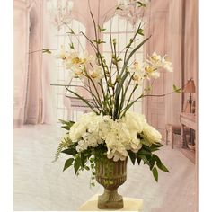 a vase filled with lots of white flowers on top of a table next to a window