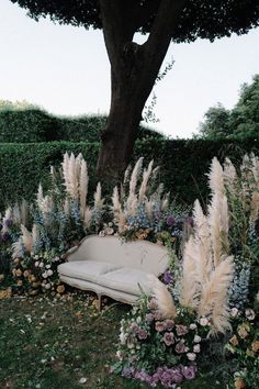 a couch sitting under a tree surrounded by flowers