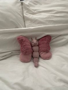 a pink stuffed butterfly laying on top of a white bed