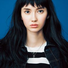 a young woman with long black hair wearing a striped shirt and jacket, looking at the camera