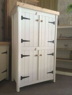 a white cabinet with black handles and drawers in a room next to a plant on the floor