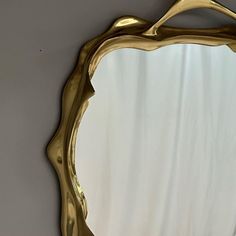 a gold mirror hanging on the wall with a white curtain in the backround