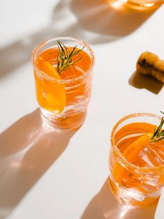 two shot glasses filled with orange juice and garnished with rosemary sprigs