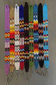 a row of colorful bracelets hanging from hooks on a gray wall next to each other