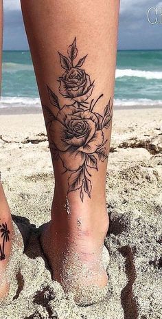 a woman's foot with flowers on it in the sand