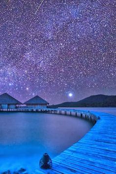 the night sky is filled with stars and bright blue water as well as some huts