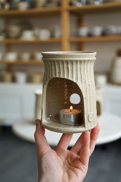 a hand holding a small candle holder with a lit candle in the center and shelves behind it