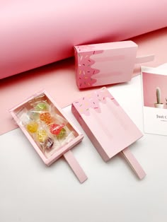 a pink box filled with assorted candies on top of a white table next to a card