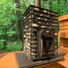 an outdoor wood burning stove on a deck in the woods with logs stacked around it