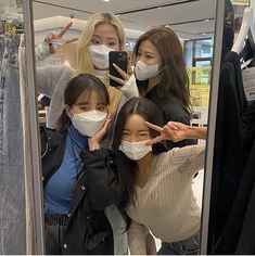 three women wearing face masks taking a selfie in front of a mirror at a clothing store