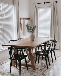 a dining room table with chairs and a vase on it in front of the window