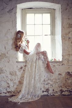 a woman sitting on a window sill in front of a white brick wall and holding a flower