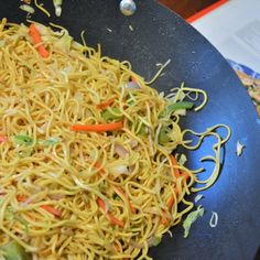 noodles are being cooked in a wok on the stove top with carrots and green peppers