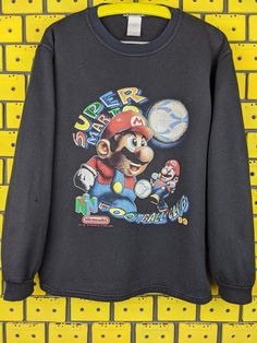 an old nintendo sweatshirt hanging on a yellow brick wall with the words super mario in it