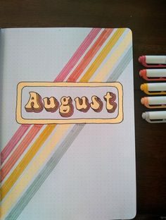 an open notebook with the word august written on it next to some crayons