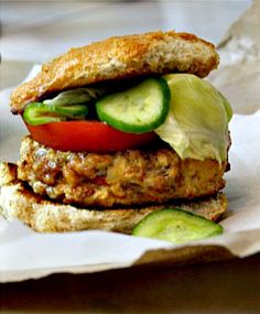 a chicken burger with lettuce and tomato on it sitting on top of wax paper