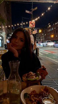 a woman sitting at a table with plates of food in front of her on the street