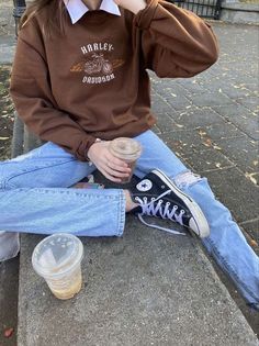 a woman sitting on the ground talking on a cell phone and drinking from a cup