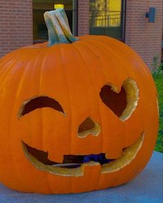 a carved pumpkin sitting on top of a cement slab in front of a brick building