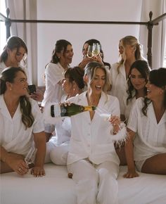 a group of women sitting on top of a bed holding wine bottles and champagne flutes