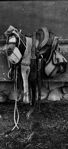 black and white photograph of cowboy's gear hanging on the side of a building