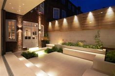 an outdoor living area is lit up at night with lights on the wall and planters in the foreground