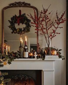 a mantel with candles, wreaths and bottles on it in front of a mirror