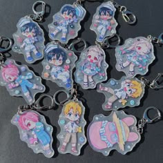 six keychains with anime characters on them sitting on a black surface in front of a gray background