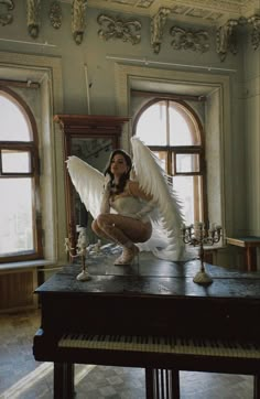 a woman dressed in white kneeling on top of a table with an angel wing over her head