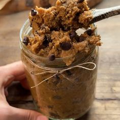 a person holding a spoon in a jar filled with cookie dough and chocolate chip cookies