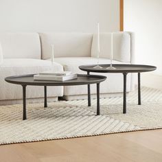 two tables sitting on top of a rug in front of a white couch