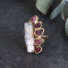 The Algae Bloom collection is inspired by growth, which can sometimes come when we least expect it; Overtaking your being in every direction and sweeping us in a new direction. This collection is about leaning into the skid and embracing change. A raw kunzite crystal is prong set and nestled against five deep red spinels embedded in brass with our organic textured ring. Length 1 1/2"This piece is handmade-to-order. Each piece will vary slightly due to the uniqueness of the stones. All metal is n Hades Jewelry, Raw Stone Rings, Algae Bloom, Water Ring, Sunburst Ring, Cascade Necklace, Kunzite Crystal, Water Rings, Raw Stone Jewelry