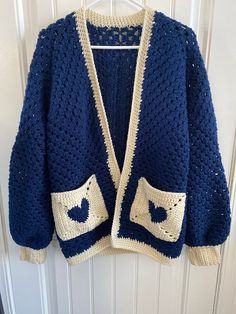 a crocheted blue jacket hanging on a white door hanger with an open front pocket