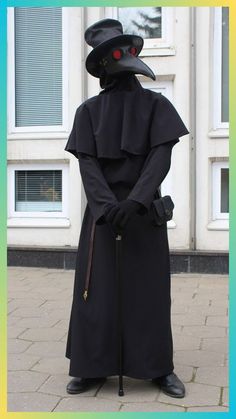 a man in a black outfit and hat with a cane standing on the sidewalk next to a building