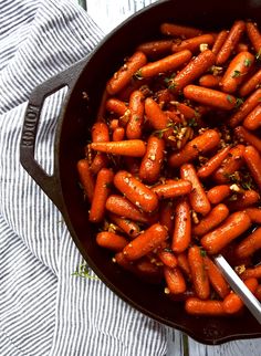 carrots are being cooked in a skillet on a table with a spoon and napkin