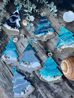 some blue and white christmas trees are on a wooden table next to seashells